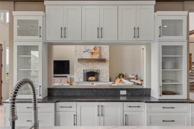 494 E Ridge Rd, Cashiers, NC 28717 - kitchen featuring white cabinetry, glass insert cabinets, dark stone countertops, and a stone fireplace