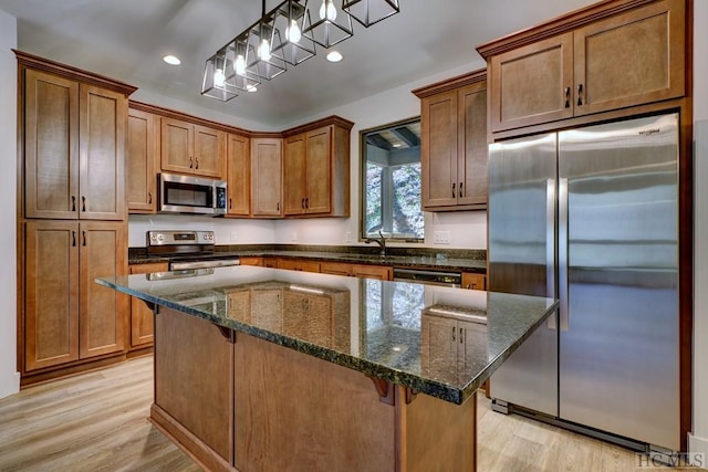 kitchen with stainless steel appliances, decorative light fixtures, a kitchen island, and dark stone countertops