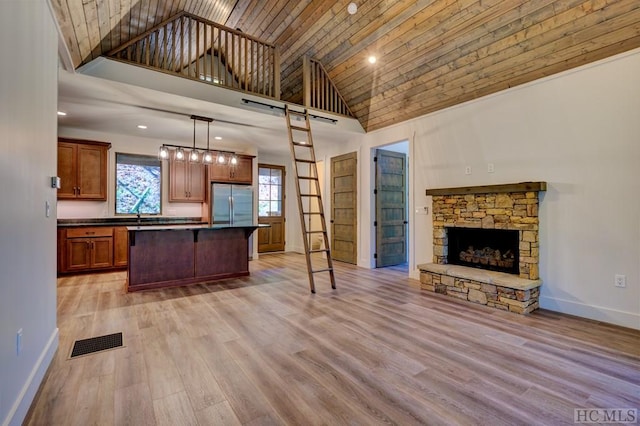 kitchen with a stone fireplace, high vaulted ceiling, light wood-type flooring, stainless steel refrigerator, and pendant lighting