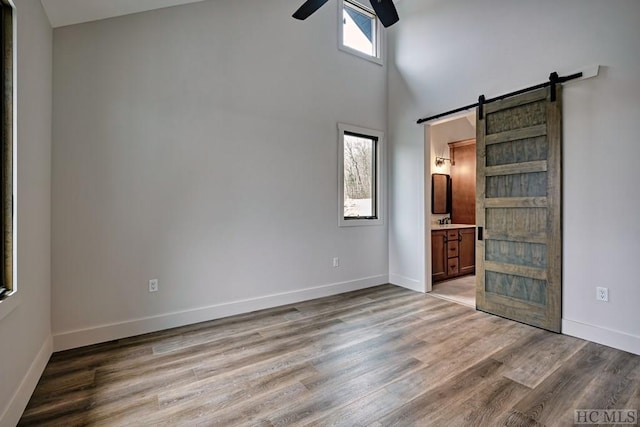 unfurnished bedroom featuring connected bathroom, ceiling fan, a barn door, hardwood / wood-style floors, and a high ceiling