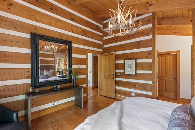 bedroom with a chandelier, wood walls, beamed ceiling, wood finished floors, and wooden ceiling