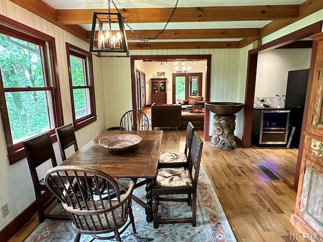 dining space with an inviting chandelier, light hardwood / wood-style flooring, beverage cooler, and beamed ceiling