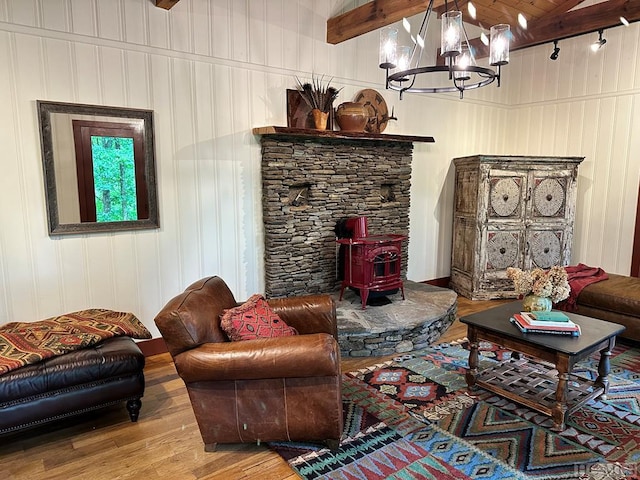 living room with hardwood / wood-style flooring, a notable chandelier, beam ceiling, and a wood stove