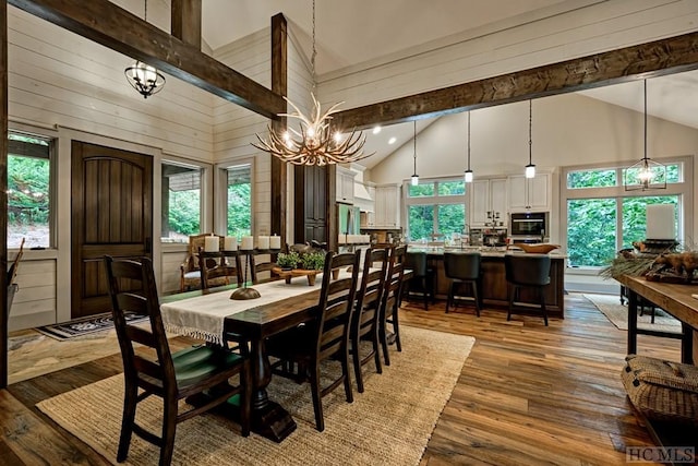 dining area with wood walls, an inviting chandelier, high vaulted ceiling, hardwood / wood-style flooring, and beamed ceiling