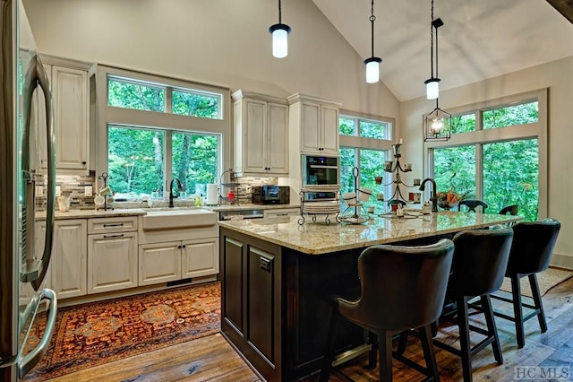 kitchen with light stone countertops, decorative backsplash, decorative light fixtures, and an island with sink