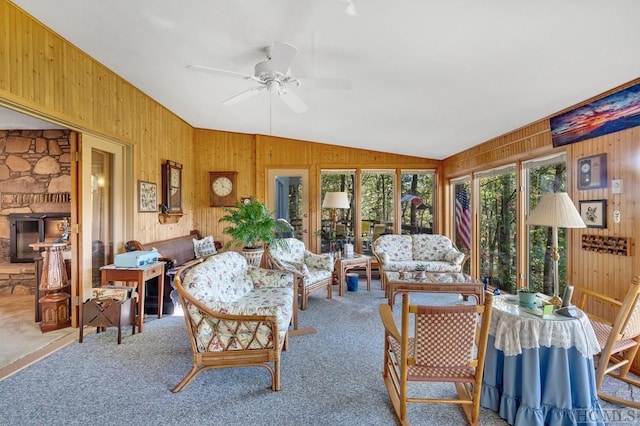 living room featuring ceiling fan, wooden walls, a fireplace, vaulted ceiling, and light colored carpet