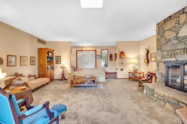 carpeted living room with a stone fireplace and a skylight