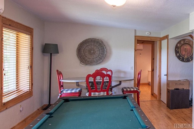 rec room with a textured ceiling, a wall unit AC, pool table, and light hardwood / wood-style floors