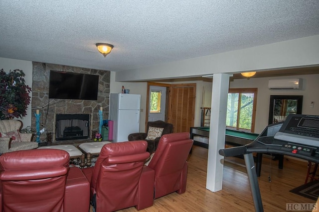 living room featuring a wall unit AC, light wood-type flooring, a textured ceiling, and a stone fireplace