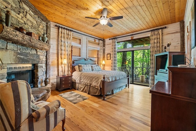 bedroom with wood ceiling, light hardwood / wood-style flooring, a stone fireplace, access to outside, and wood walls