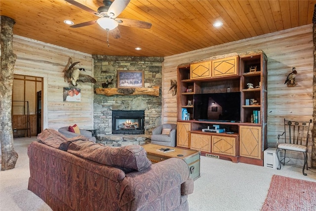 living room featuring a stone fireplace, wood walls, carpet flooring, ceiling fan, and wooden ceiling