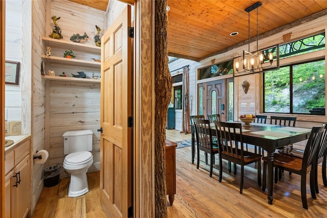 dining room with wooden walls, wooden ceiling, and light wood-type flooring