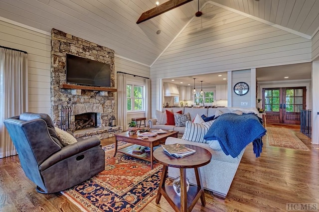 living room with high vaulted ceiling, hardwood / wood-style flooring, wood walls, and a stone fireplace