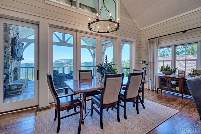 dining space with a water view, wood-type flooring, a notable chandelier, and wood walls