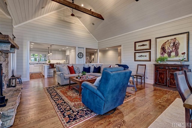 living room featuring hardwood / wood-style floors, a stone fireplace, beamed ceiling, high vaulted ceiling, and sink