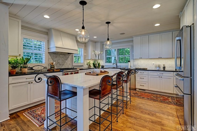 kitchen with decorative light fixtures, premium range hood, a center island, white cabinetry, and light wood-type flooring