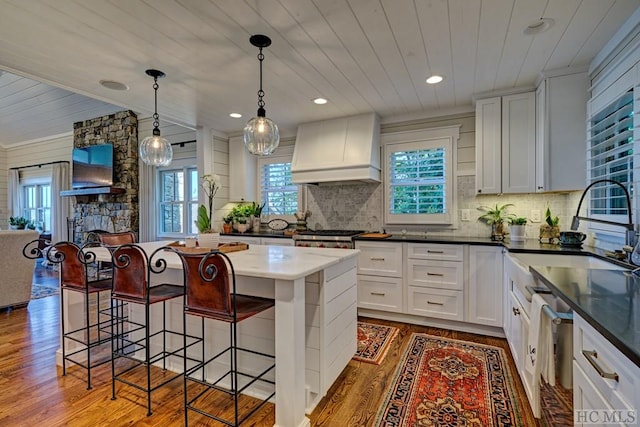 kitchen with custom exhaust hood, wood-type flooring, a kitchen island, white cabinets, and dishwashing machine