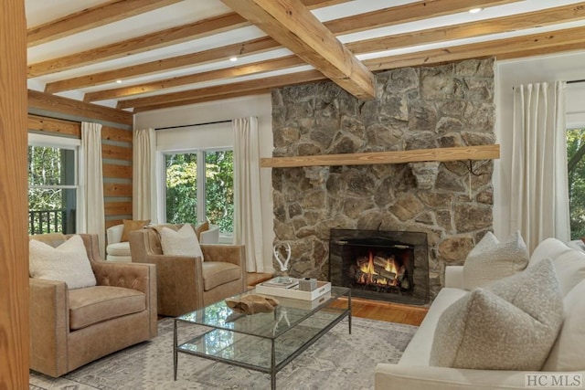 living room featuring beamed ceiling, a stone fireplace, and light wood-type flooring