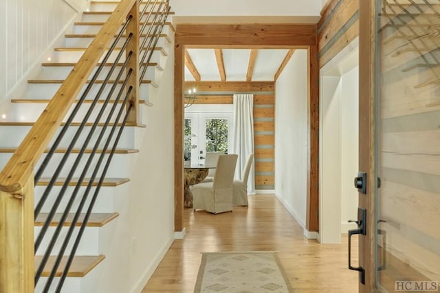 interior space featuring beamed ceiling, wood walls, french doors, and light hardwood / wood-style flooring