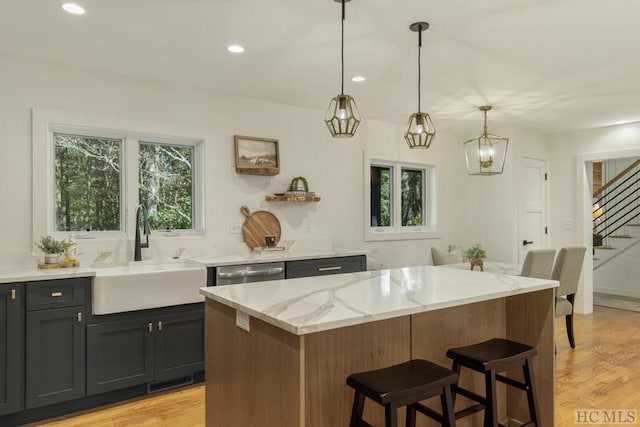 kitchen with sink, light hardwood / wood-style flooring, light stone countertops, a kitchen island, and decorative light fixtures