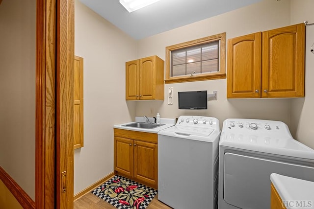 laundry room featuring cabinets, washing machine and dryer, sink, and light hardwood / wood-style floors