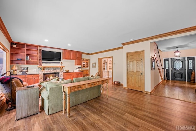 living room with ornamental molding, a stone fireplace, and light hardwood / wood-style flooring