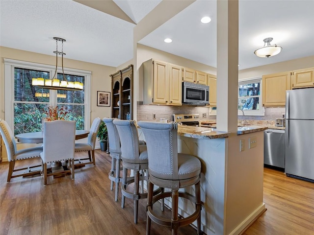 kitchen with stainless steel appliances, a kitchen bar, wood finished floors, and light brown cabinets