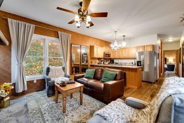 living room featuring wooden walls, ceiling fan with notable chandelier, and light wood finished floors