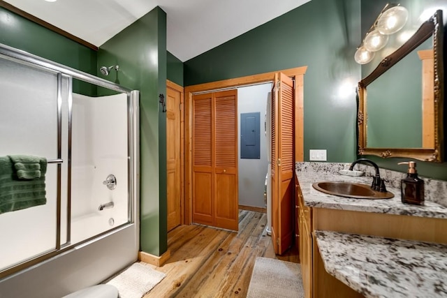 bathroom featuring vanity, wood finished floors, electric panel, bath / shower combo with glass door, and vaulted ceiling