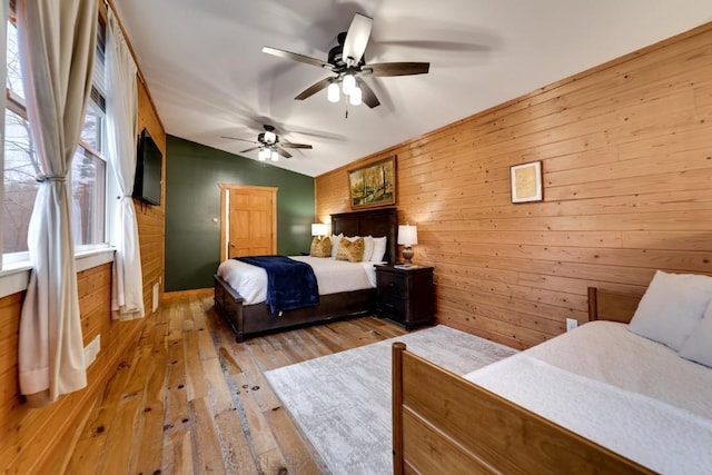 bedroom featuring wood walls, light wood-style floors, lofted ceiling, and ceiling fan