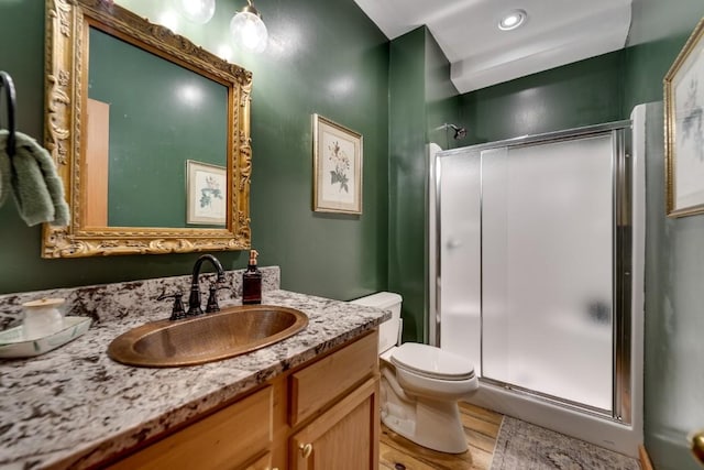 full bath featuring toilet, a stall shower, vanity, and wood finished floors