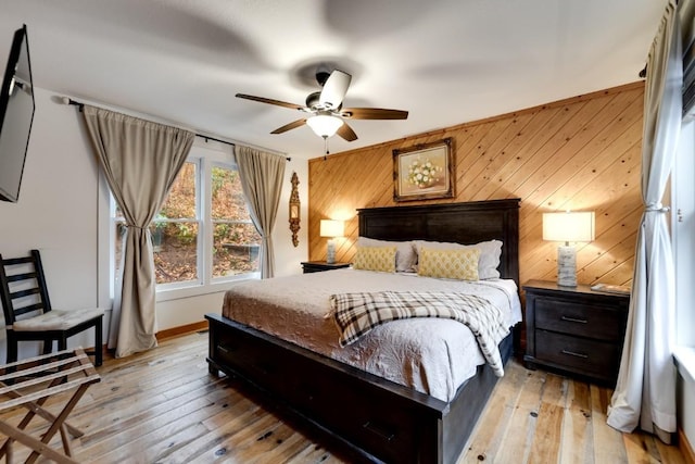 bedroom featuring baseboards, wooden walls, a ceiling fan, and light wood-style floors