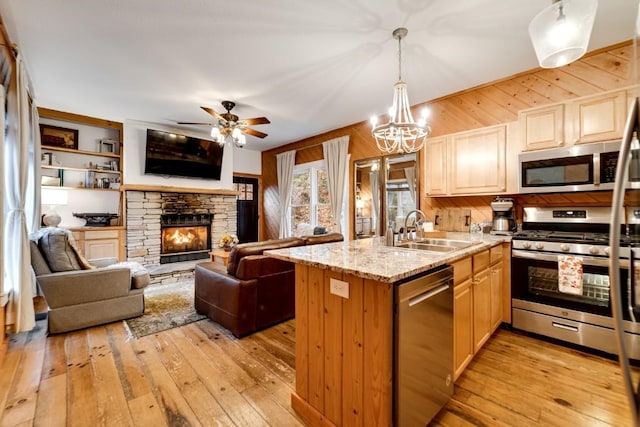 kitchen featuring light wood-type flooring, a sink, light stone counters, appliances with stainless steel finishes, and a peninsula