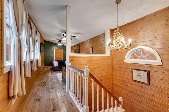 hall with an upstairs landing, an inviting chandelier, hardwood / wood-style floors, and wood walls