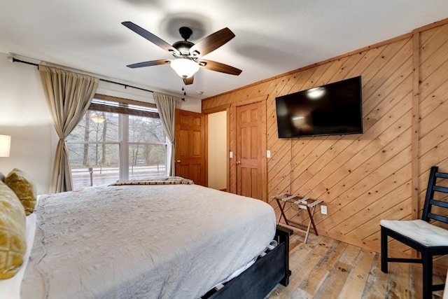 bedroom with wooden walls, a ceiling fan, and light wood finished floors