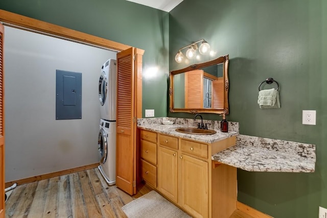 bathroom with stacked washer and clothes dryer, electric panel, wood finished floors, baseboards, and vanity