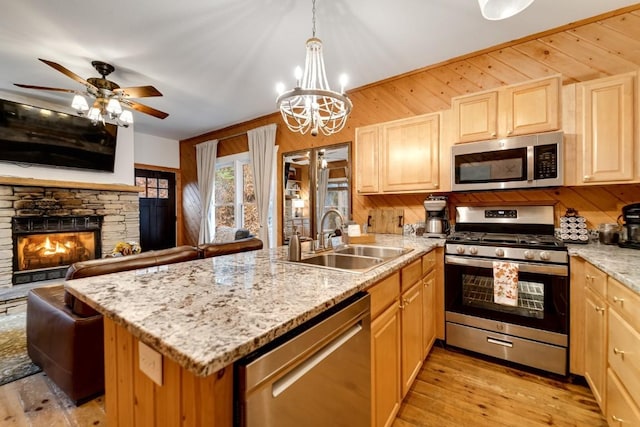 kitchen with wooden walls, a peninsula, a sink, appliances with stainless steel finishes, and light wood-type flooring