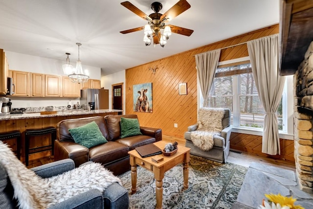 living room featuring wood finished floors, wood walls, and ceiling fan with notable chandelier