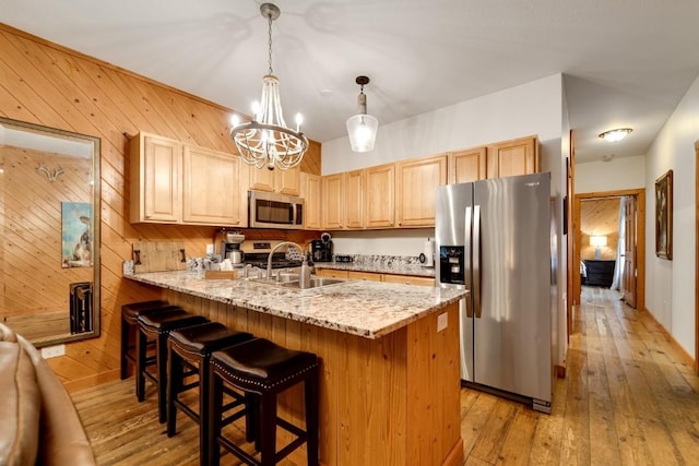 kitchen with light brown cabinets, light wood-style flooring, a sink, appliances with stainless steel finishes, and a notable chandelier