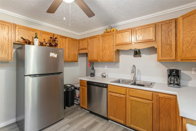 kitchen with stainless steel appliances, a sink, a textured ceiling, light countertops, and light wood-type flooring