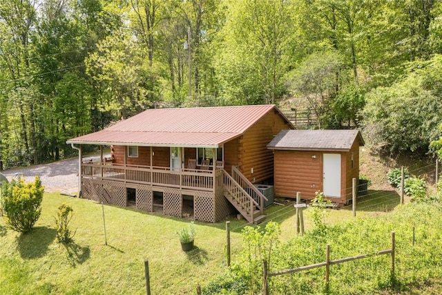 back of property featuring covered porch, a lawn, log siding, and a storage shed