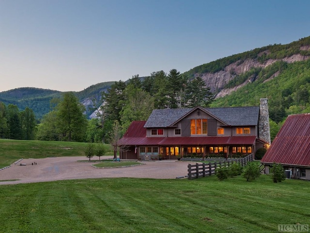 back of property with a chimney, a mountain view, metal roof, and a lawn