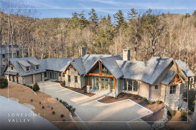 view of front facade featuring stone siding, driveway, a chimney, and french doors