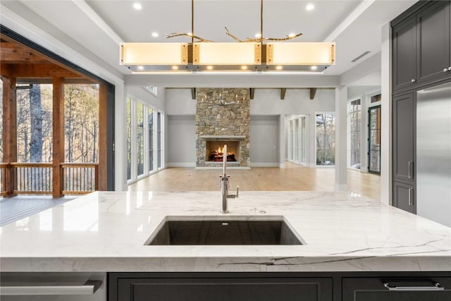 kitchen with light stone counters, open floor plan, built in refrigerator, a stone fireplace, and a sink