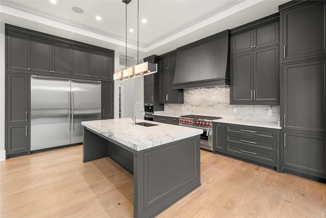 kitchen with light stone counters, light wood-style flooring, premium range hood, a sink, and high end appliances