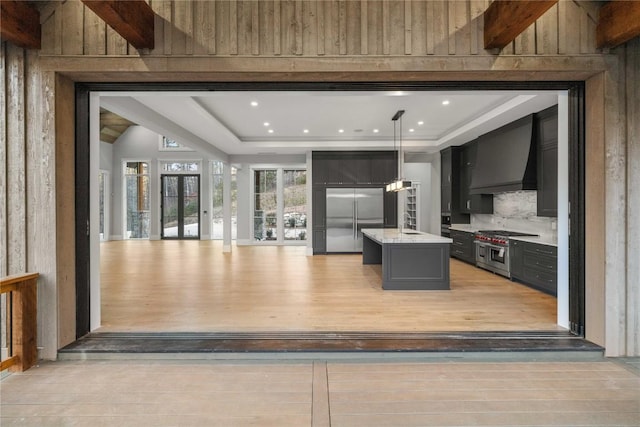 kitchen with light wood-style flooring, a sink, high end appliances, a raised ceiling, and custom range hood