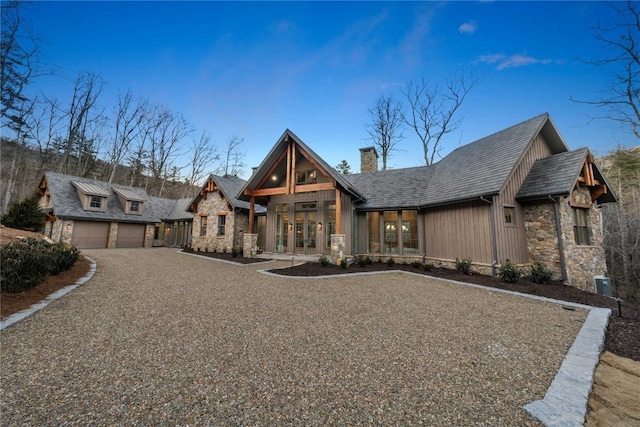 view of front of property with stone siding, a chimney, an attached garage, gravel driveway, and french doors