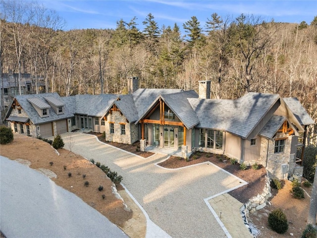 view of front of house with gravel driveway, stone siding, a chimney, and french doors