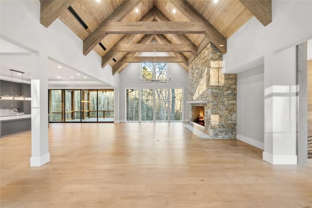 unfurnished living room with high vaulted ceiling, light wood-style floors, wood ceiling, a stone fireplace, and a chandelier