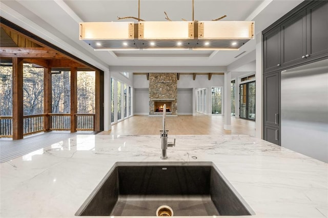 kitchen with open floor plan, a sink, a stone fireplace, light stone countertops, and stainless steel built in refrigerator